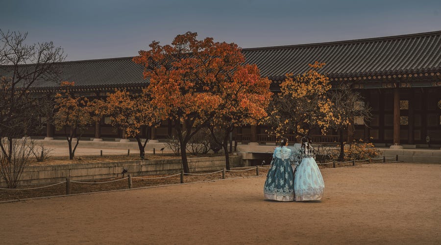 Duas pessoas vestidas com trajes tradicionais conversando sobre o calendário coreano nos jardins de um templo.