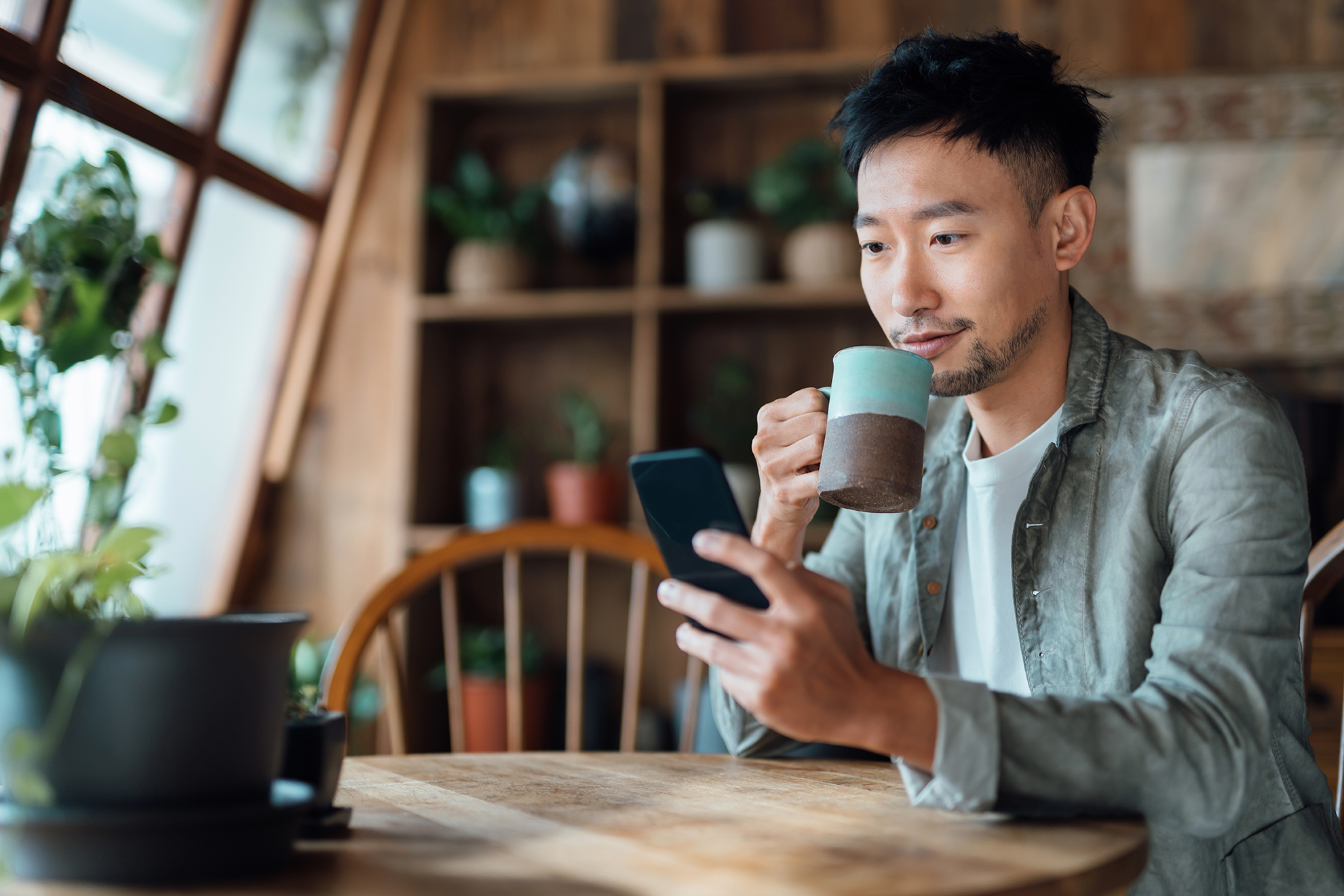 Homem tomando um café enquanto confere sua agenda no celular para as aulas do curso de japonês no RJ.