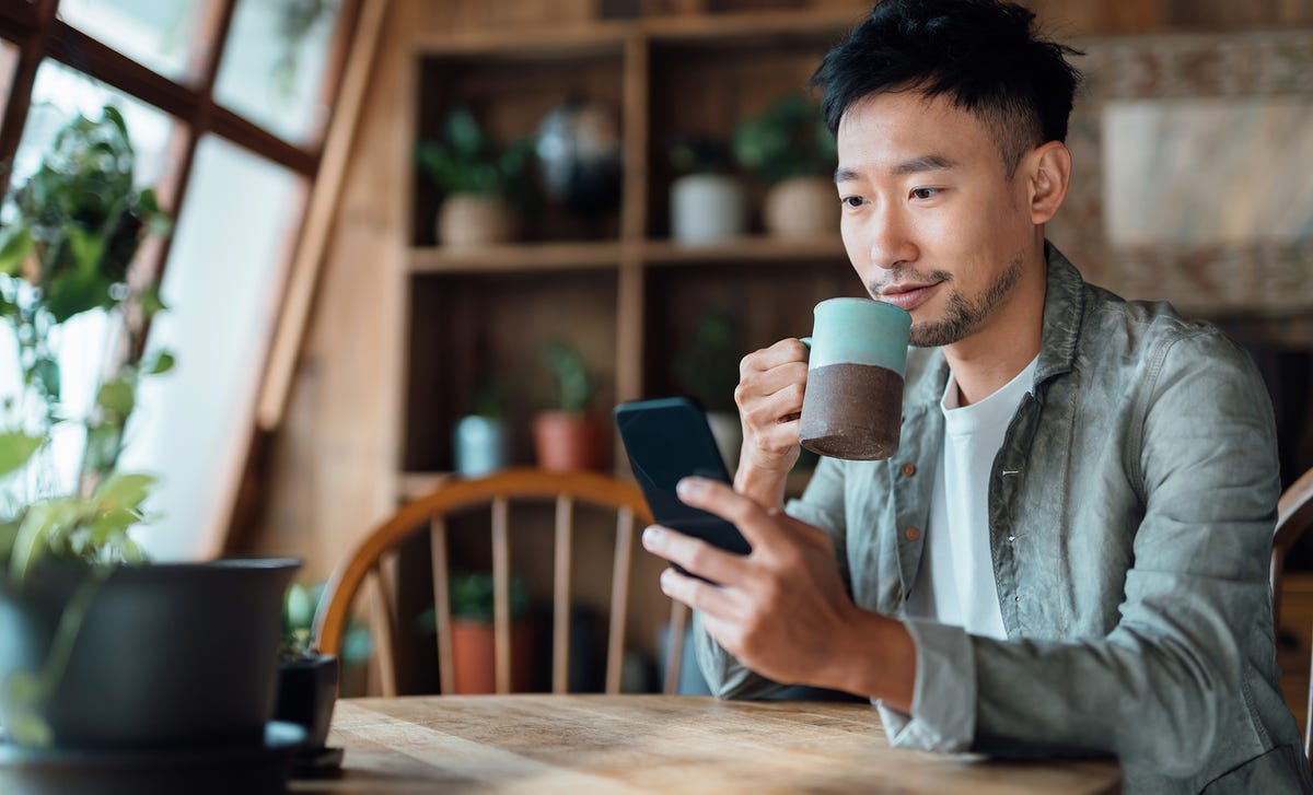 Homem tomando um café enquanto confere sua agenda no celular para as aulas do curso de japonês no RJ.