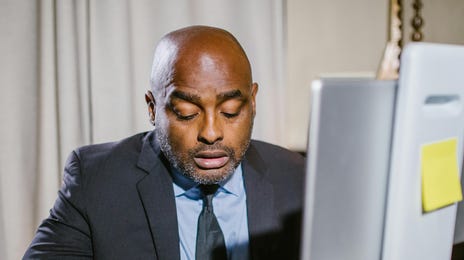 Homem negro com trajes sociais escrevendo o que está aprendendo do idioma romeno.