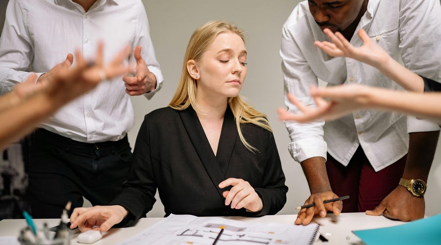 Mulher em seu trabalho com diversas pessoas falando em volta, o que pode gerar erros de comunicação entre a equipe.