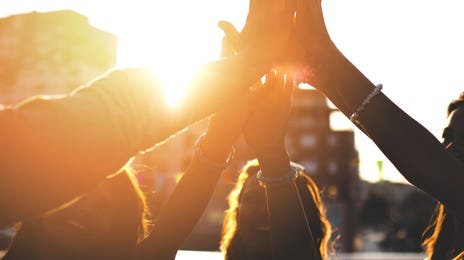 Estudantes de intercâmbio reunidos em um high-five no pôr do sol.