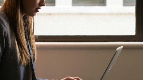 Mulher mexendo em seu laptop com roupa social enquanto aprende com as lições do MyBerlitz Speaking Tutor.