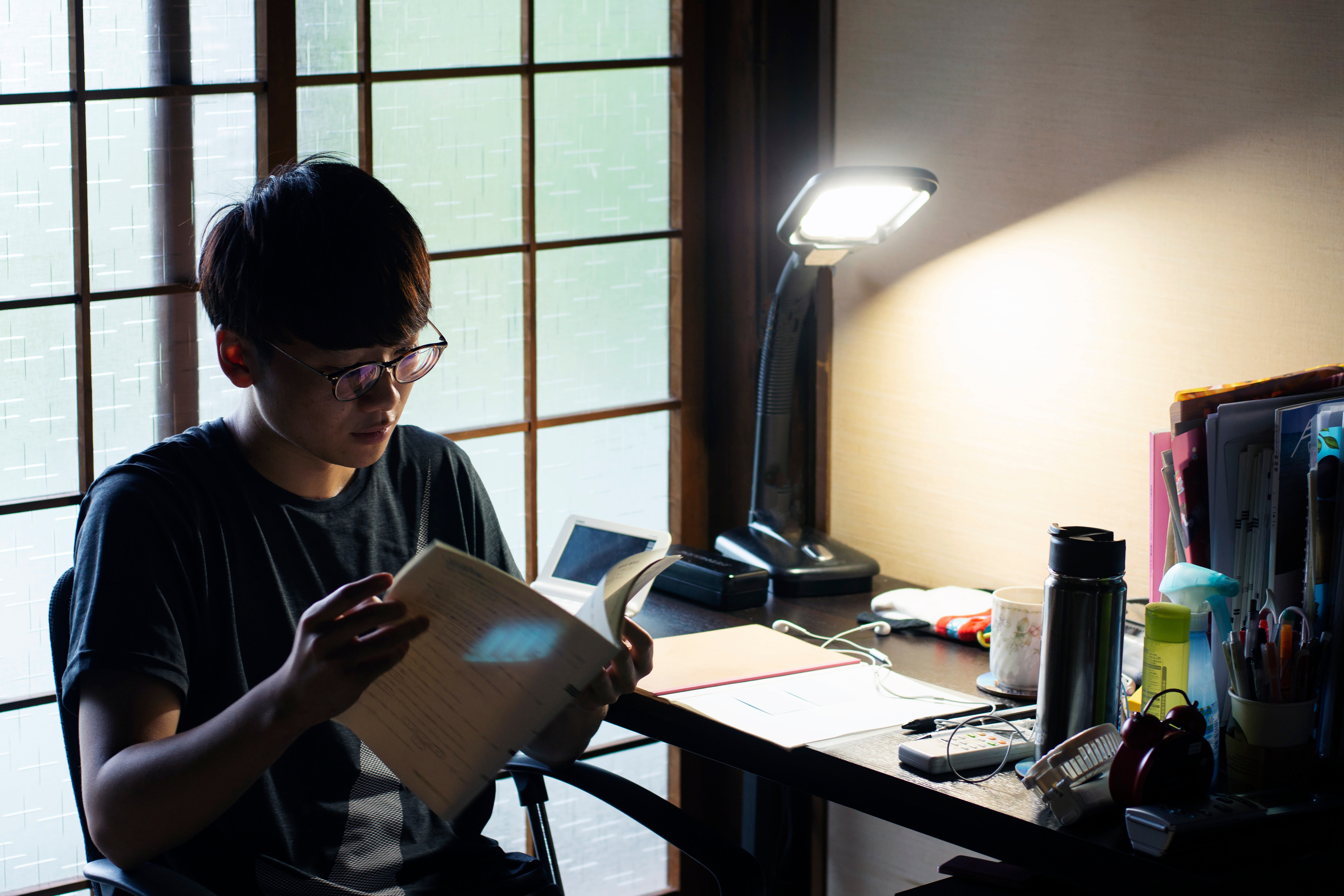 Menino asiático lendo um livro em sua escrivaninha.