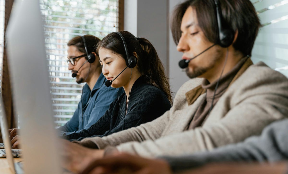 Uma mulher e dois homens trabalhando com atendimento ao cliente, usando fones de ouvido e computadores para ganhar produtividade digital.