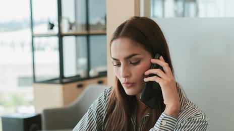 Mulher em uma ligação e anotando em um caderno, pois o gerenciamento de tempo é importante para definir prioridades.