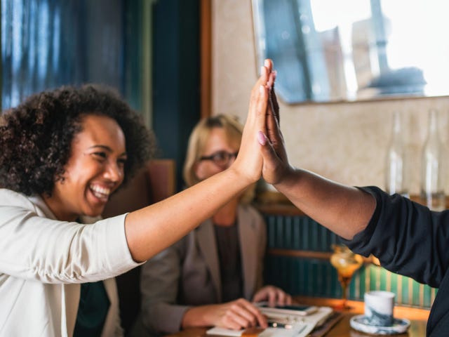 Pessoas fazendo um high five sentados em uma mesa de café.