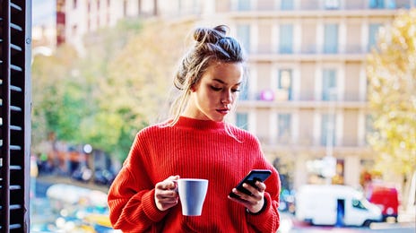 Mulher de cabelo preso segurando um café enquanto mexe no celular.