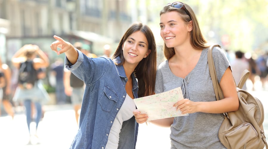 Uma menina ajudando outra garota com o caminho em um mapa, representando o tema "fazer intercâmbio".