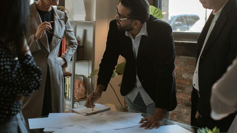 Equipe de homens e mulheres reunidas em volta de uma mesa com papeis, discutindo ideias na academia de negócios.