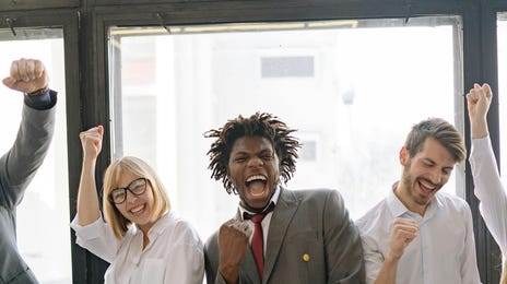 Homens e mulheres adultos do meio corporativo comemorando com sorrisos e gestos os avanços que fizeram na escola de negócios do Berlitz.
