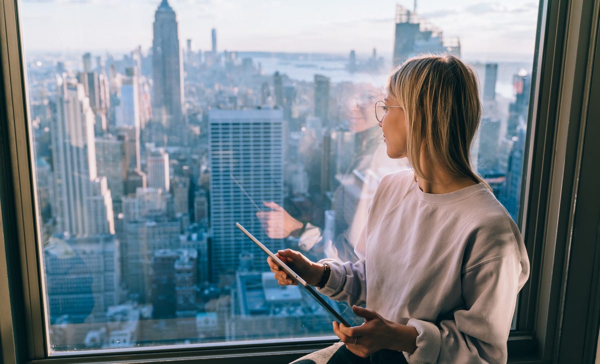 Mulher de cabelo claro olhando pela janela a cidade de Nova York, cidade incluída nos programas de intercâmbio do Berlitz.
