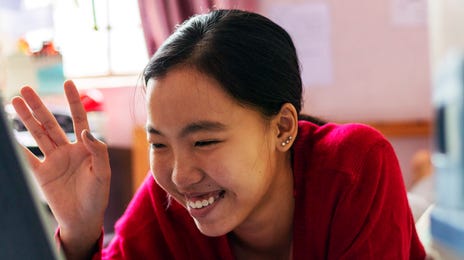 Mulher sorrindo e acenando enquanto mexe em seu computador.