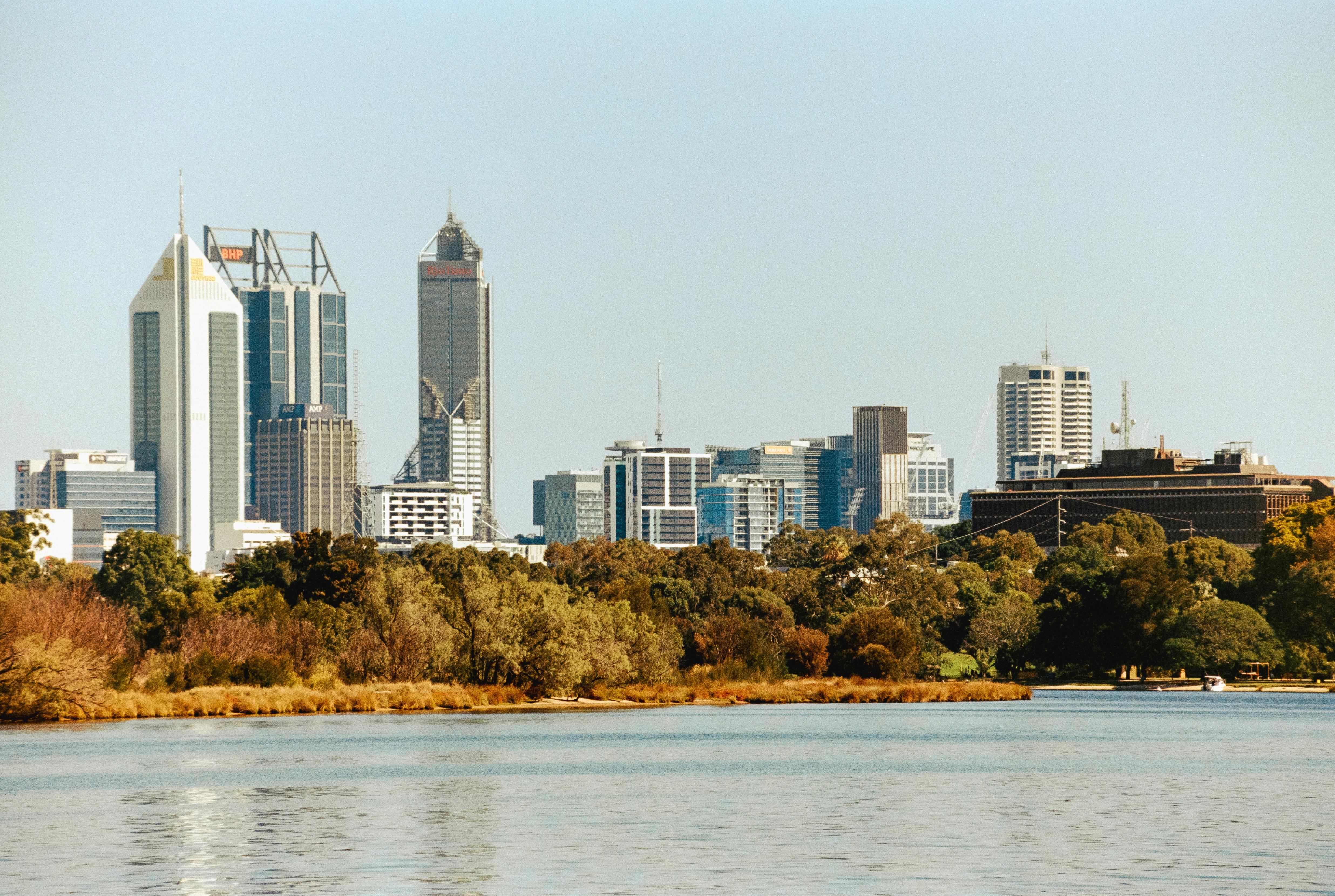 Vista da cidade de Perth, na Austrália, com bosques ao lado de um lago e edifícios.