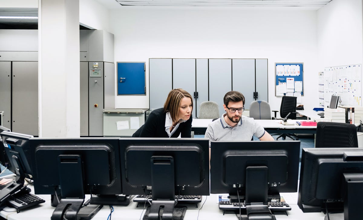 Duas pessoas da área de tecnologia aprendendo inglês em sala com computadores.