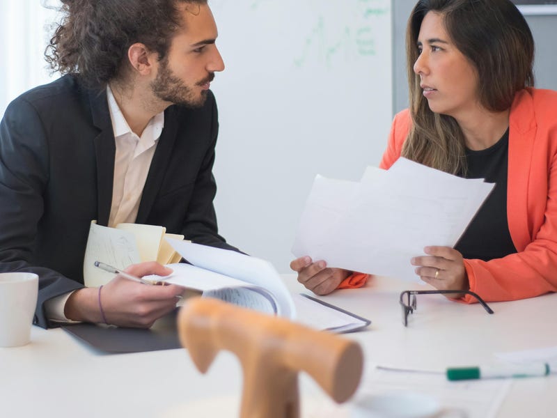 Mulher de cabelo comprido e homem com o cabelo cacheado preso em um coque durante uma de suas reuniões one on one.