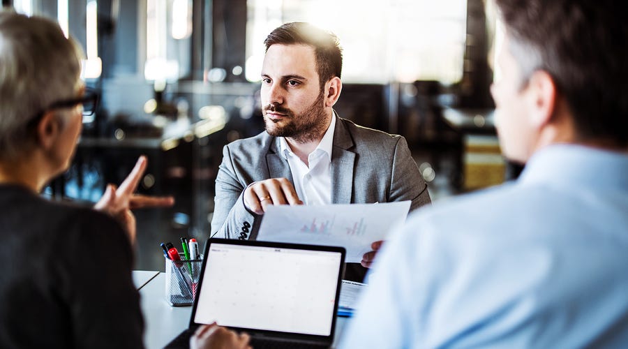 Três colaboradores reunidos para analisar gráficos sobre o desempenho da administração estratégica das lideranças.