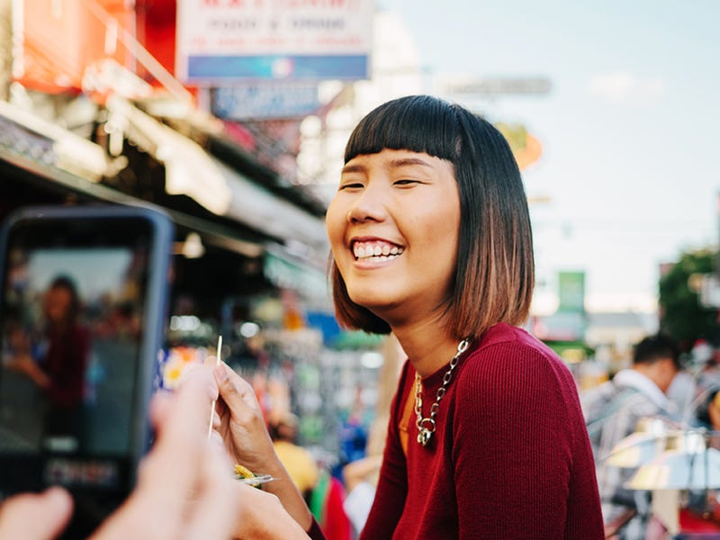 Homem está tirando uma foto da namorada, que sorri, enquanto aproveita suas férias em inglês no exterior.