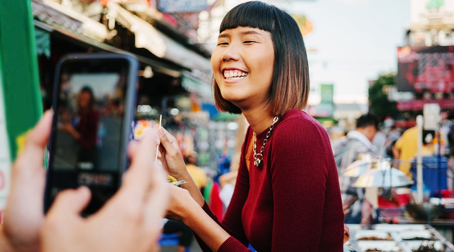 Homem está tirando uma foto da namorada, que sorri, enquanto aproveita suas férias em inglês no exterior.