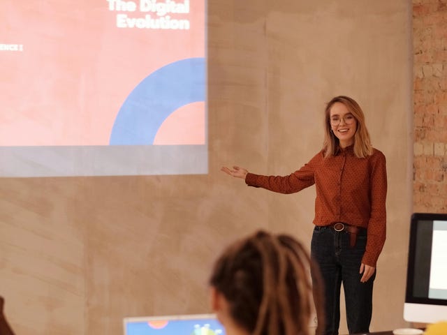 Mulher simula uma palestra com slides para um grupo de estudantes do curso de apresentação.