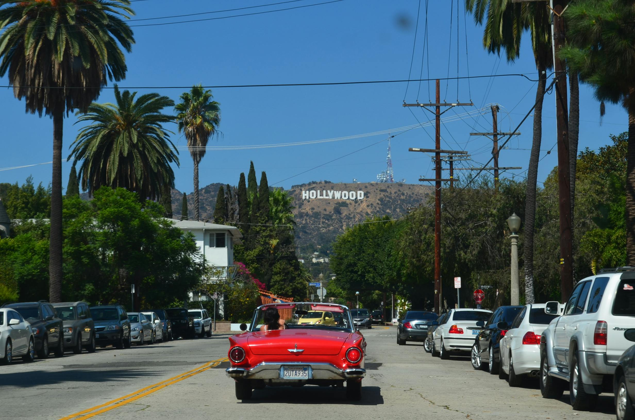 Carro vermelho andando pelas ruas de Los Angeles, nos Estados Unidos, com o letreiro de Hollywood no horizonte.
