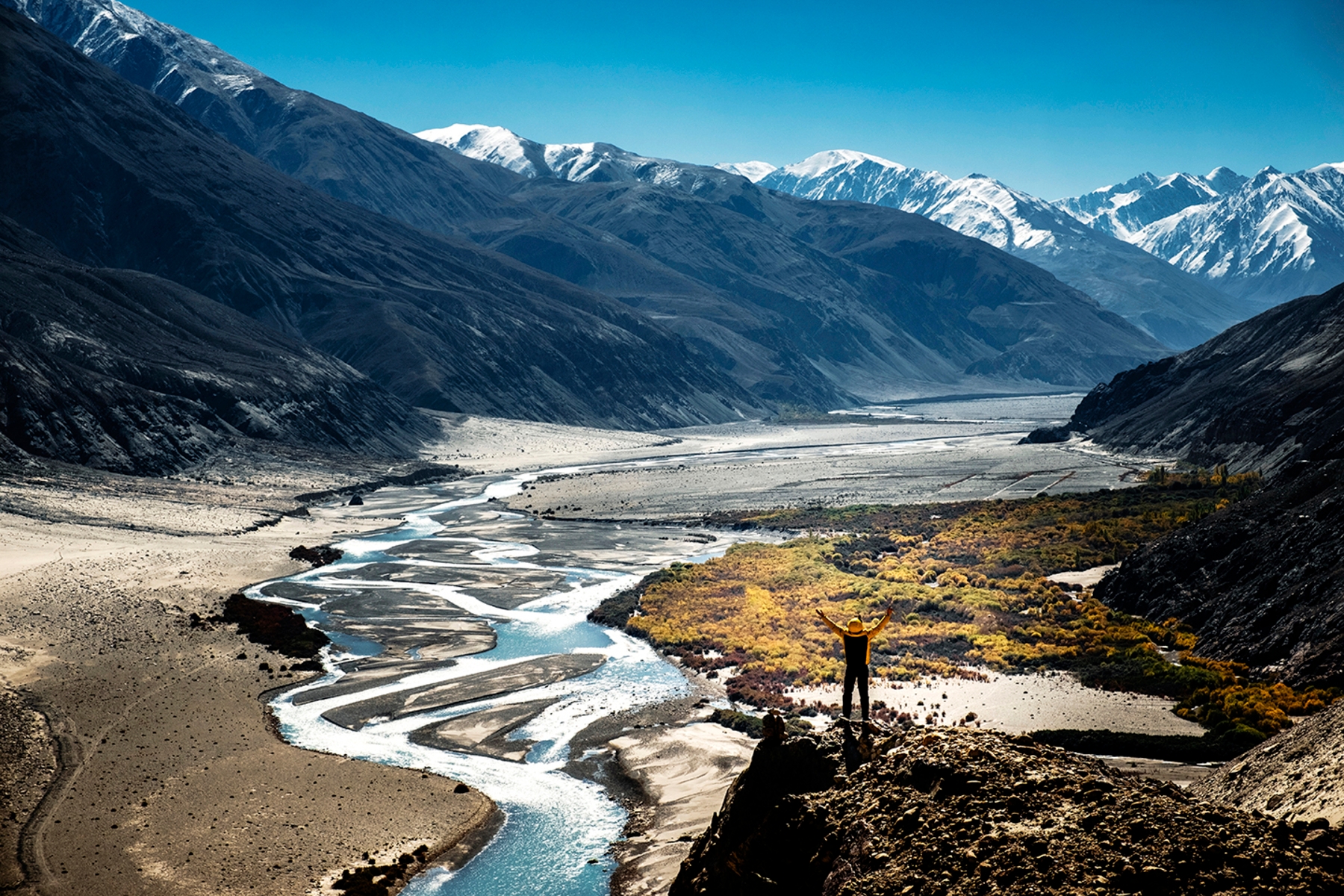 Homem viajante admirando a paisagem intocada de montanhas nevadas e riachos enquanto pensa nos nomes de geografia em espanhol para cada elemento.