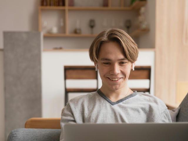 Garoto loiro jovem em sua casa estudando pelo computador com fones de ouvido sem fio.