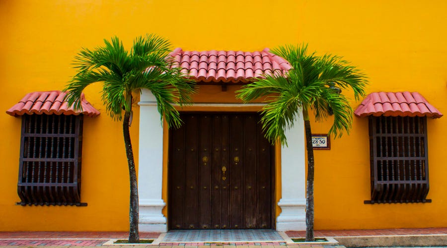 Partes da casa em espanhol de uma residência amarela com duas palmeiras na porta de entrada.