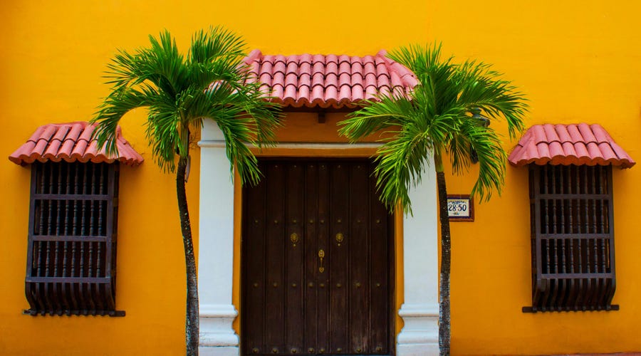Partes da casa em espanhol de uma residência amarela com duas palmeiras na porta de entrada.