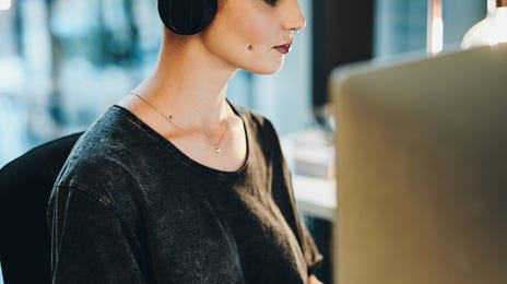 Mulher de fones mexendo no computador.