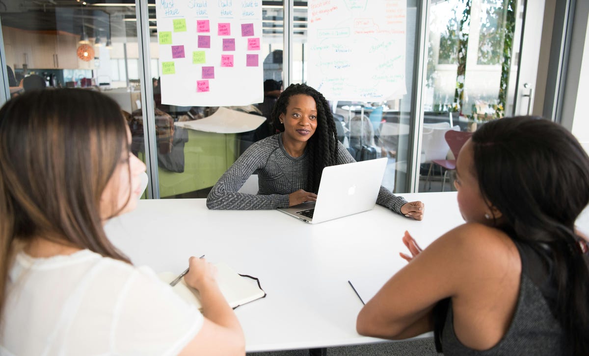Colaboradora negra recebendo um feedback construtivo de suas superiores em uma reunião descontraída.