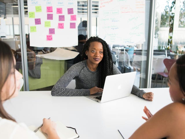 Colaboradora negra recebendo um feedback construtivo de suas superiores em uma reunião descontraída.