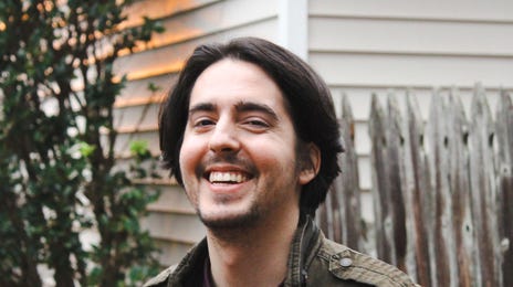 Homem sorrindo com roupas quentes do lado de fora de casa.