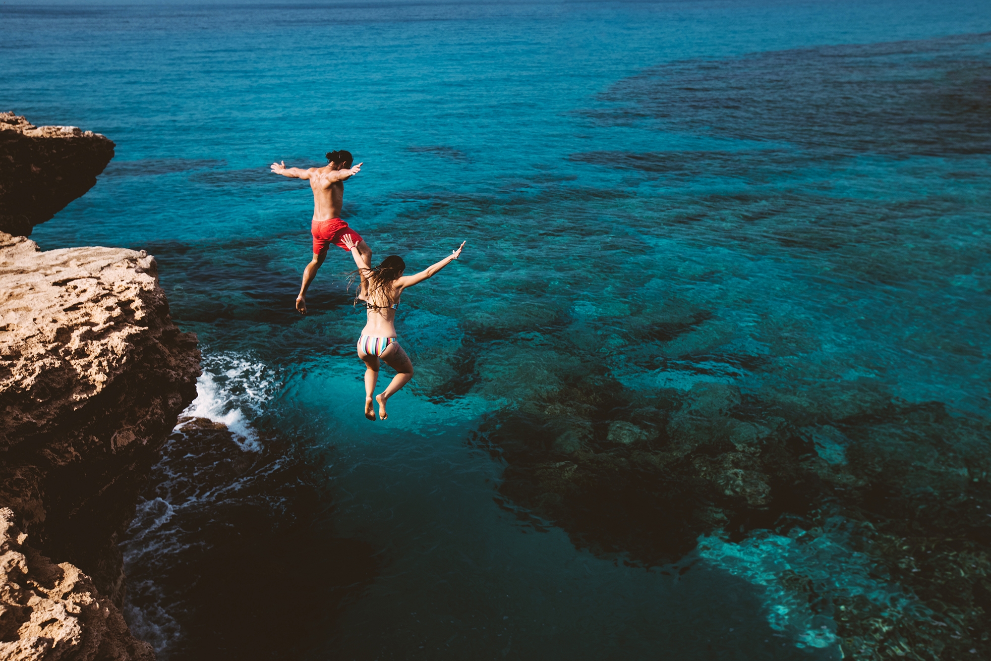 Amigos se divertindo pulando no mar azul enquanto estudam no intercâmbio Malta.