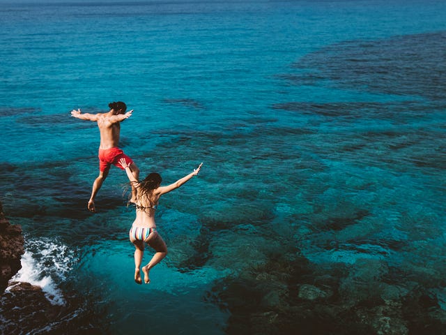 Amigos se divertindo pulando no mar azul enquanto estudam no intercâmbio Malta.