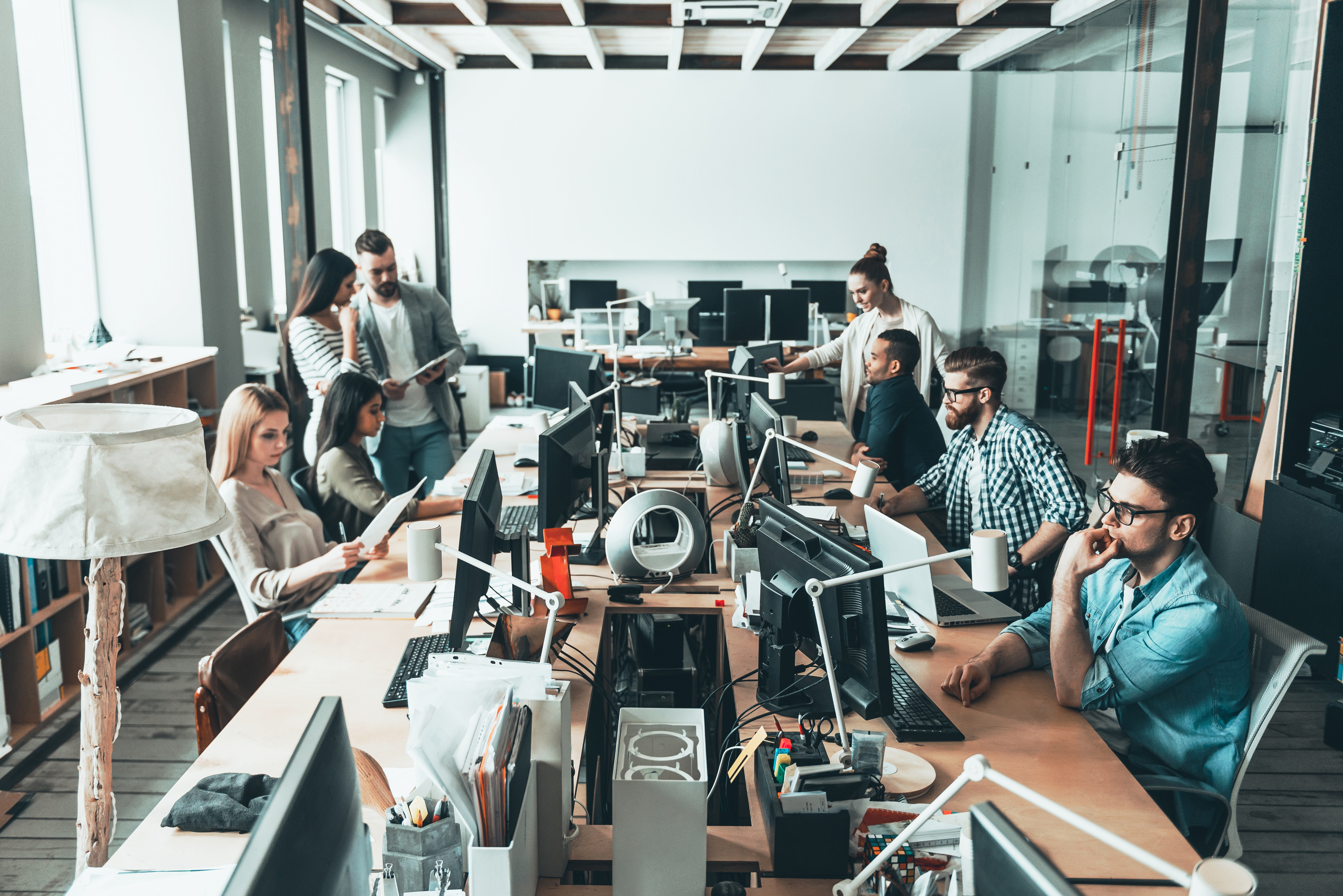 Mesa com diversos computadores e pessoas conversando e mexendo nestes computadores.