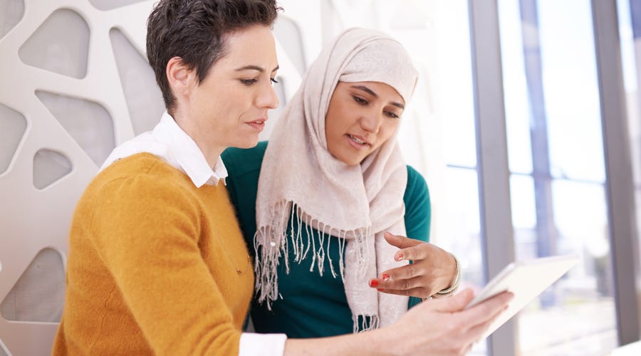 Mulheres debatendo enquanto uma delas mostra algo em um tablet.