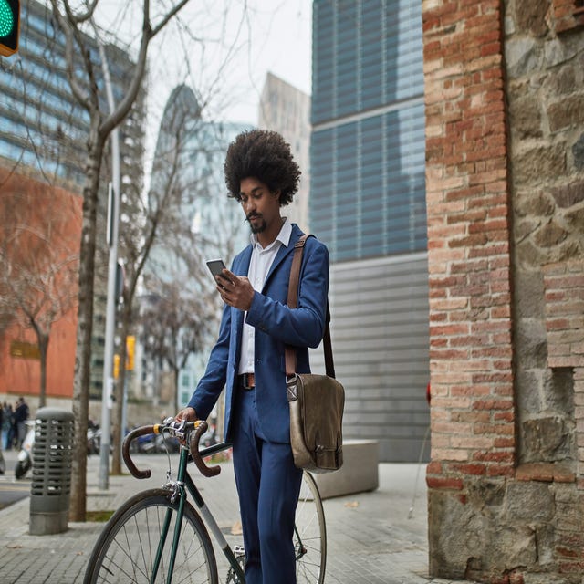 Homem negro parado em uma rua de Berlim, segurando sua bicicleta enquanto verifica sua nota do exame Telc b2 no celular.