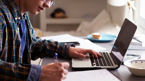 Menino fazendo anotações de algo que está vendo no computador.