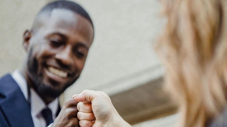 Funcionário negro recebe um feedback construtivo de sua chefe e tocam as mãos em harmonia.
