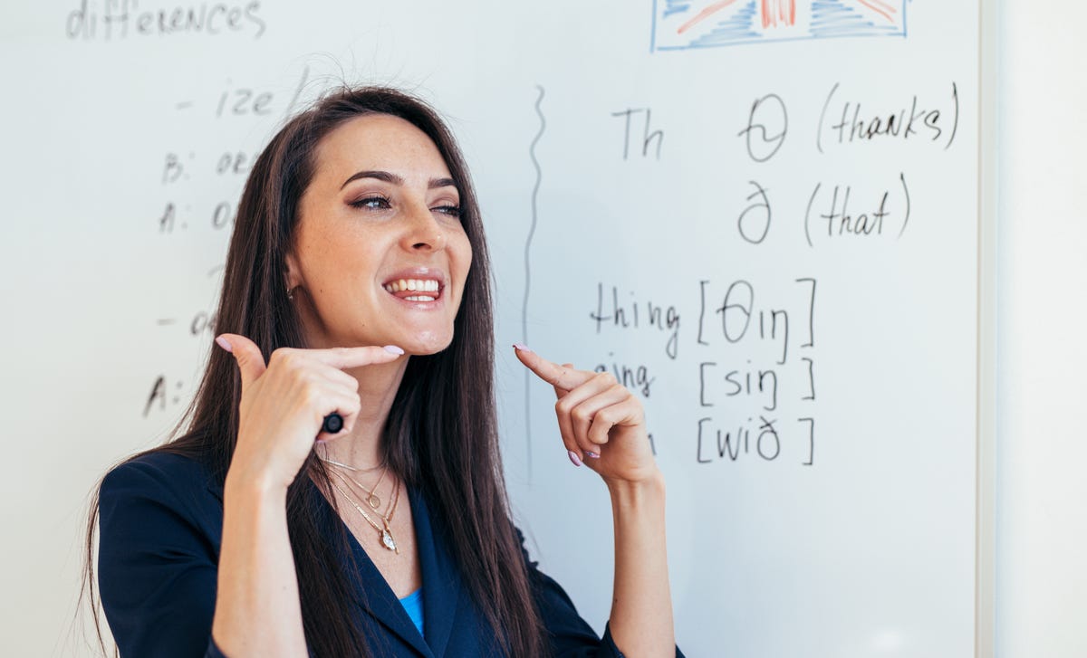 Mulher ao lado de uma lousa ensinando inglês na escola de idiomas Berlitz.