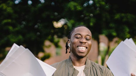 Homem negro feliz com papeis em suas mãos da matrícula do Berlitz da Haddock Lobo.