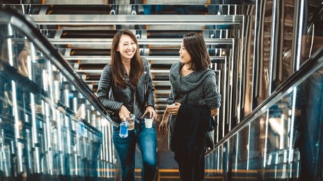 Mulheres sorrindo enquanto sobem uma escada rolante.