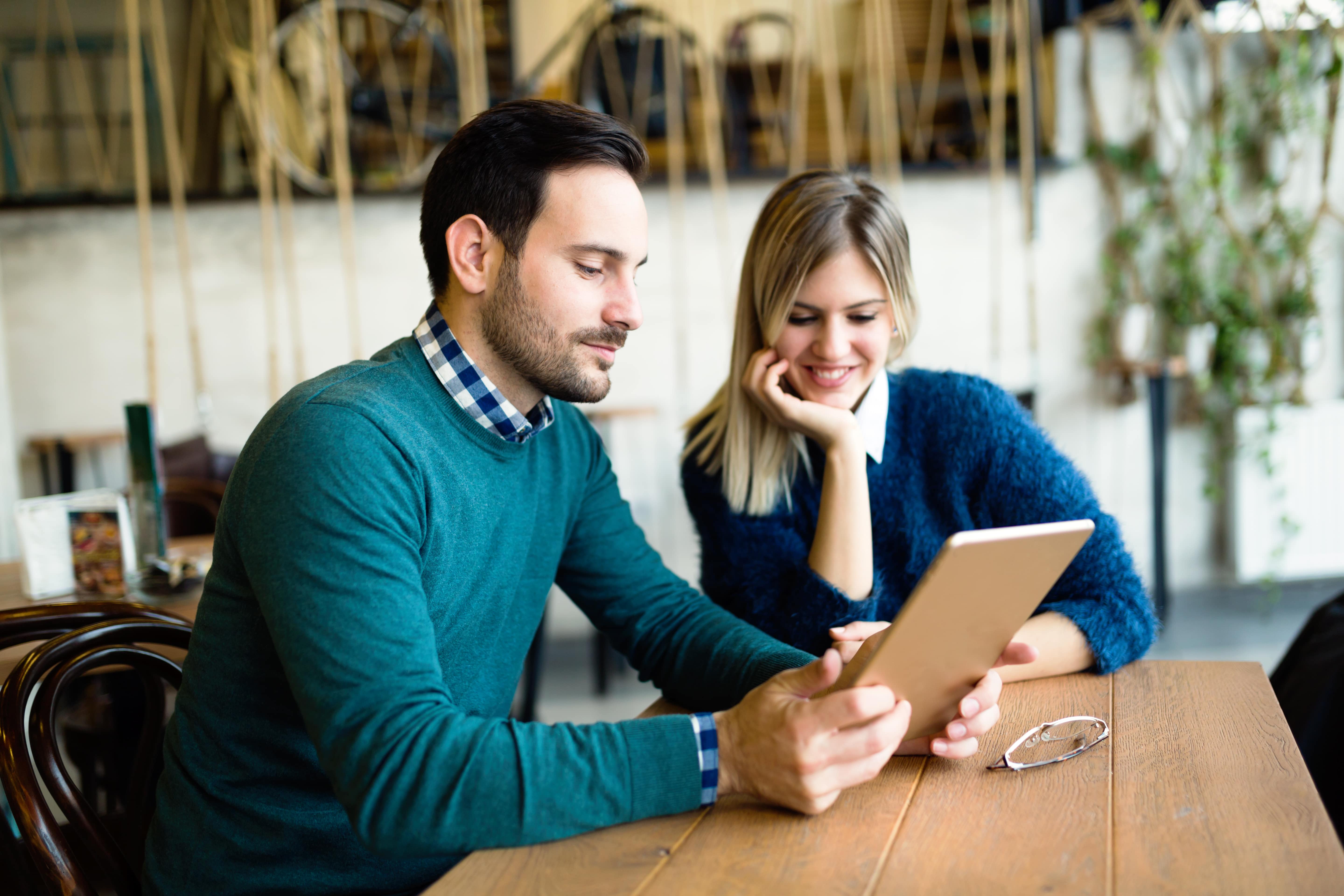 Um homem e uma mulher estudam juntos, por um tablet em uma cafeteria, para o exame Telc a2.