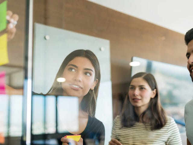 Equipe colando post-its em uma tabela de vidro para organizar as ideias de projeto, usando os métodos ágeis.
