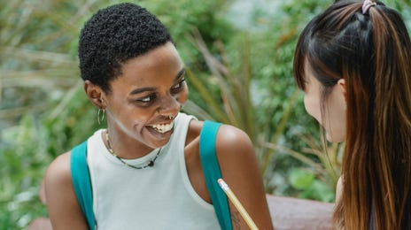 Duas estudantes de idiomas conversam sorridentes sobre o aprendizado virtual.