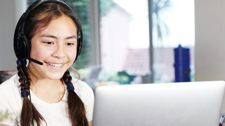 Menina de headphones em frente a um laptop durante uma aula online.