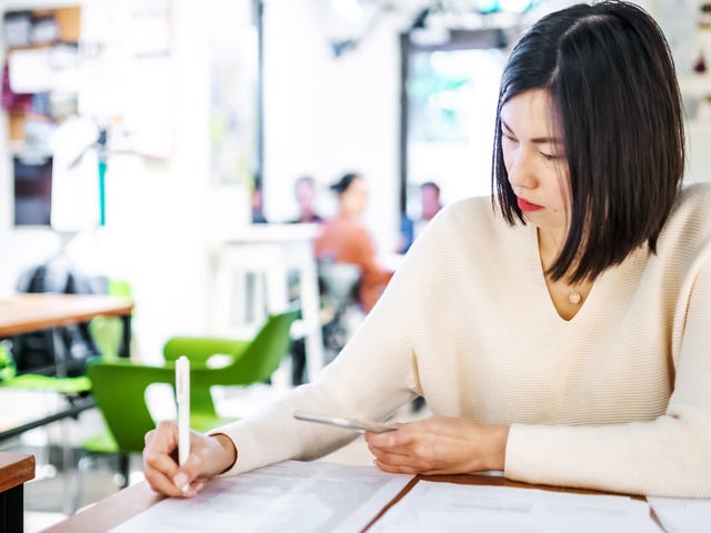 Mulher asiática escrevendo em um caderno.