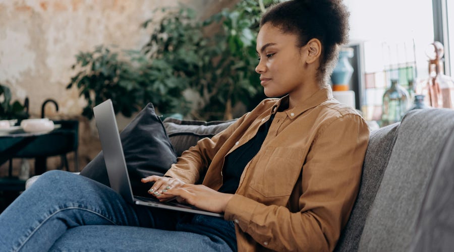 Mulher sentada no sofá estudando os níveis de espanhol em seu laptop.