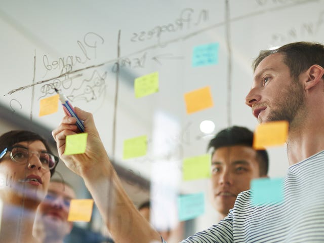 Equipe adicionando informações em uma lousa cheia de post-its.